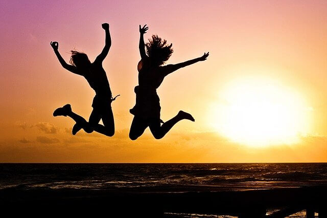 友人同士が日没のビーチでジャンプしている写真